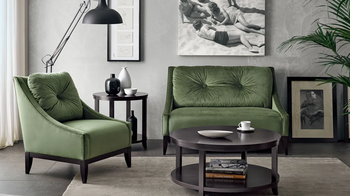 Salottino in stile contemporaneo americano. Divano a due posti e poltrona in velluto verde, abbinati a tavolini porta lampada e centro sala rotondi in legno scuro